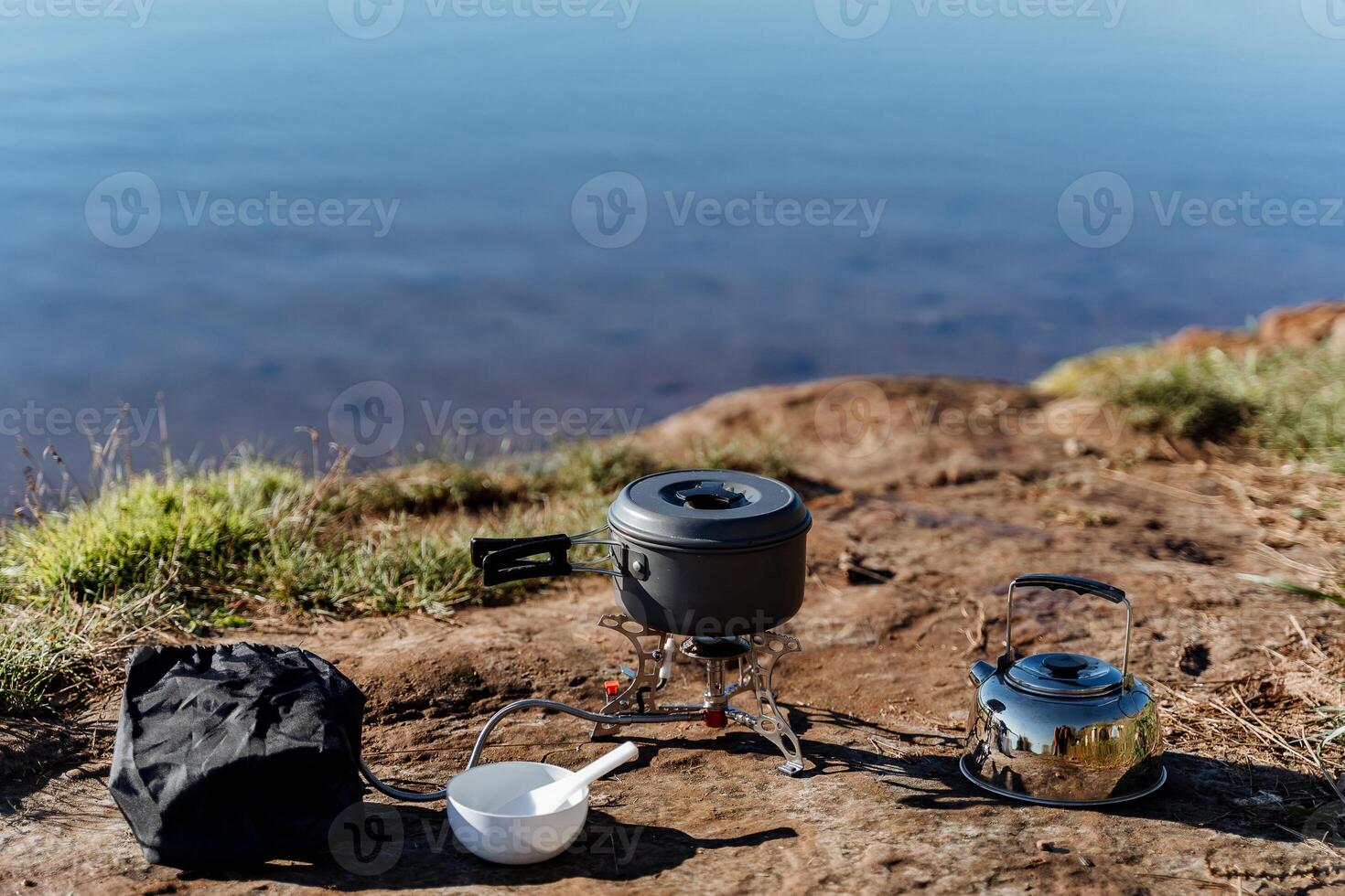 cooking on a gas burner in nature, gas camping stove for cooking food, aluminum pot with a lid stands on the burner, camping equipment for cooking. photo