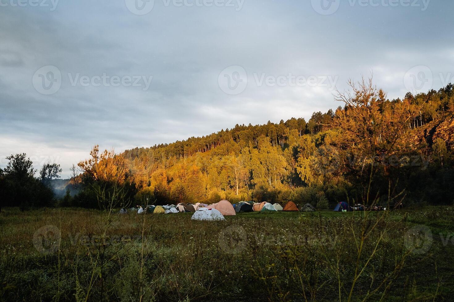 Tent camp on the river Bank, colorful tents stand in the field, morning in a tourist camp, cloudy weather on a hike, travel organization, overnight in nature photo