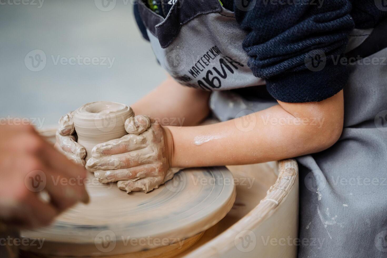 The child is engaged in a potter's wheel. Pottery Workshop. sculpt from the clay pot. creativity for children. fine motor skills of the hands. four hands. photo