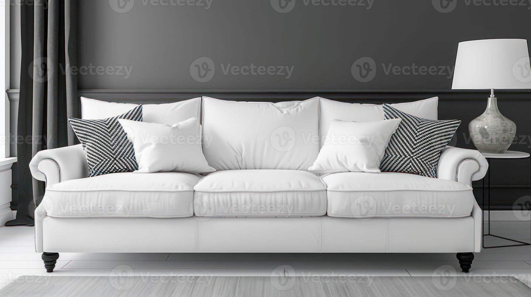 A white sofa with patterned pillows sits in front of a grey wall, with a lamp and side table on the right. photo