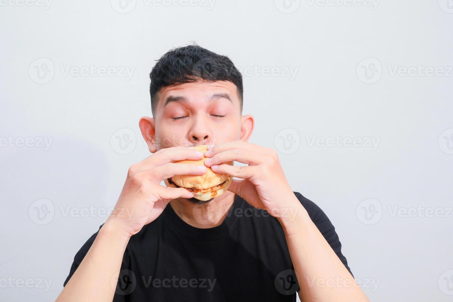 portrait of a young asian man is eating hamburger, isolated on white background. Fast food advertising photo