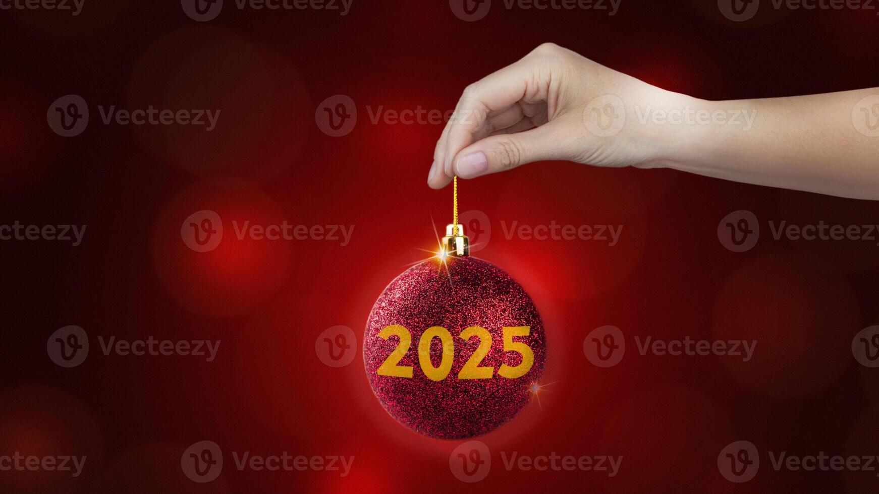 Red Christmas ball with yellow 2025 in woman's hand on red background, horizontal New year style banner photo
