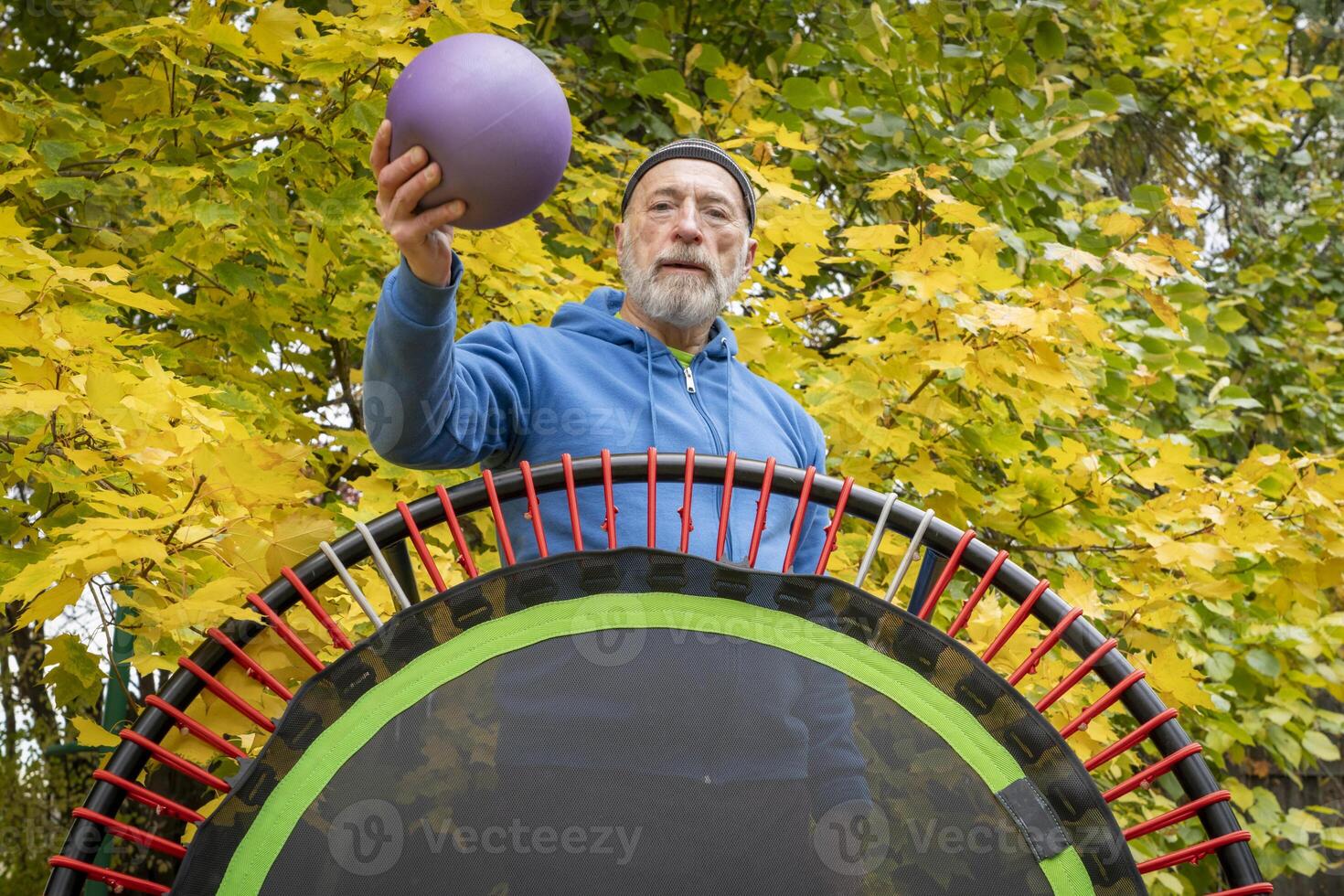 senior man with a medicine ball and a mini trampoline for fitness exercising and rebounding, fall backyard scenery photo