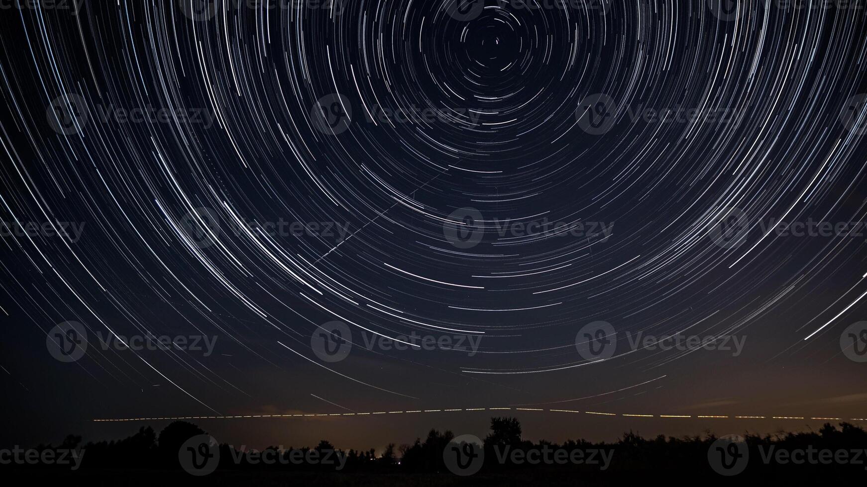 Star trails in the night sky. Stars move around a polar star. Silhouettes of trees photo