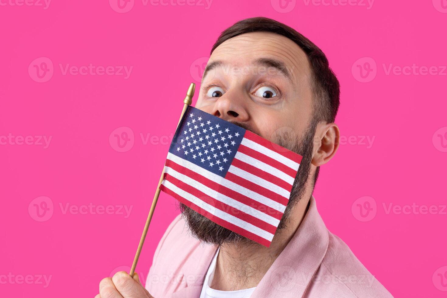 Portrait of a satisfied young man with a beard with an American flag on a red studio background. Great US patriot and defender of freedom. photo