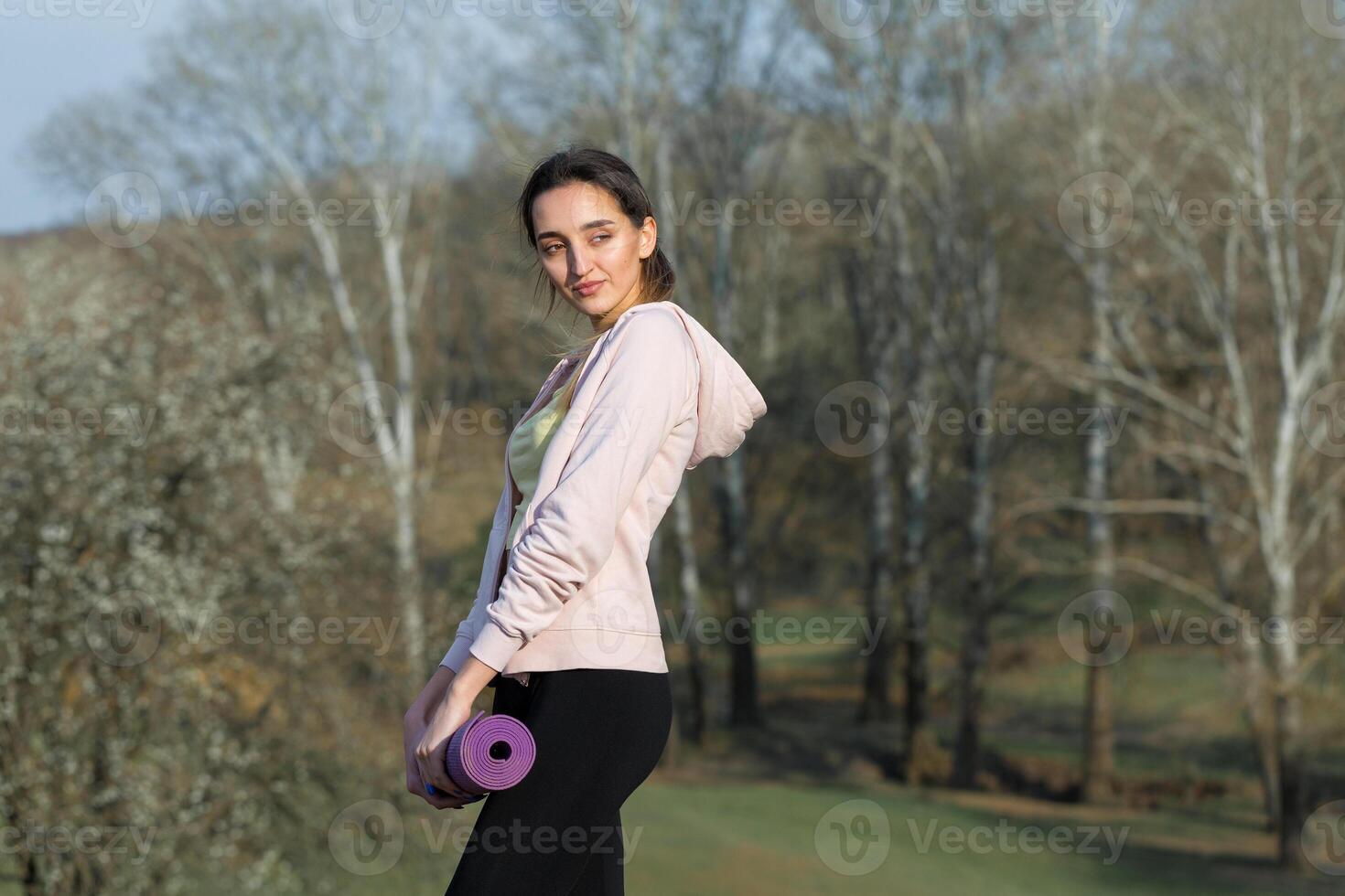 A young slim athletic girl in sportswear performs a set of exercises. Fitness and healthy lifestyle against the background of green spring pasture hills. photo
