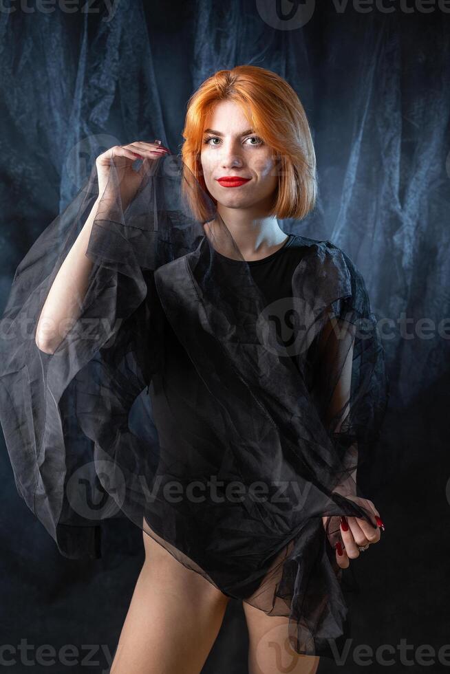 A young red-haired girl in a black bodysuit poses in the studio against a dark background. photo