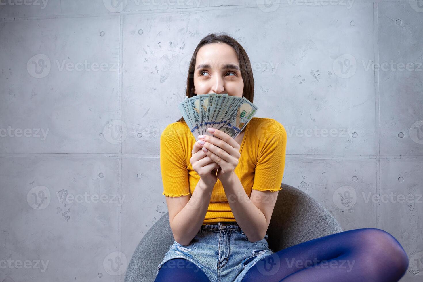 Photo of a wealthy woman in simple clothes holding a fan of dollar money isolated against a concrete wall background