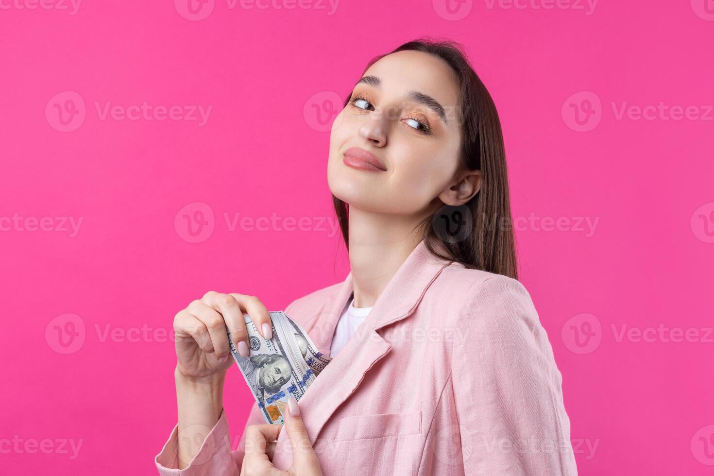 A woman in a pink jacket holds dollar banknotes, a puzzled business girl hides dollars standing on a red background. photo