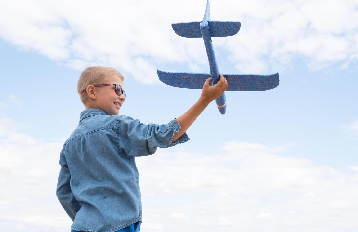 Happy child playing with a toy airplane against a blue sky in an open field photo