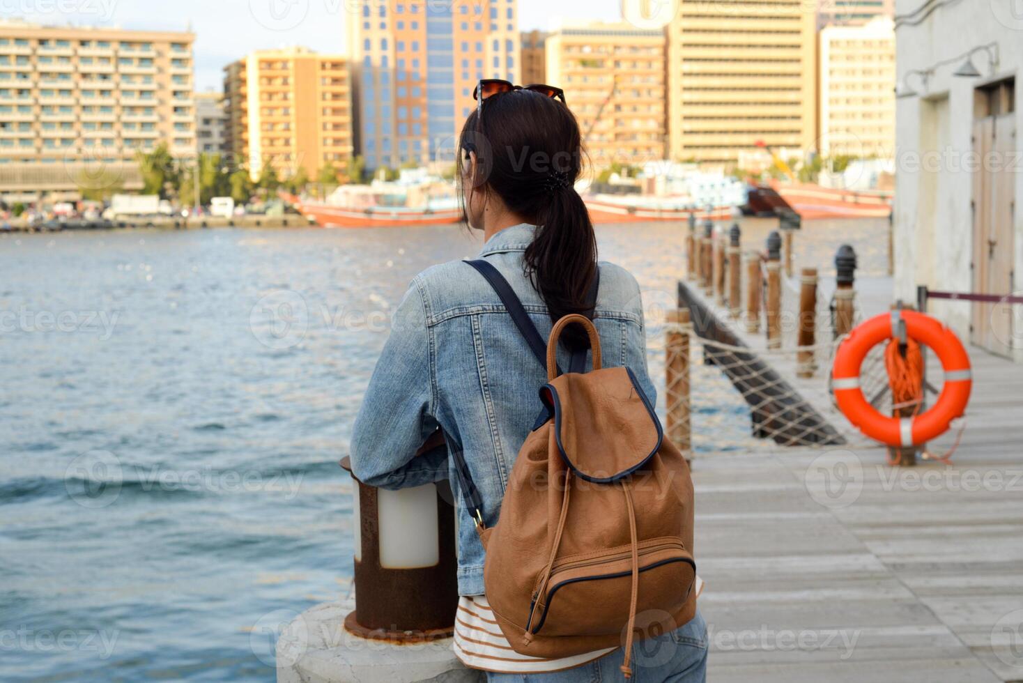 A young woman with a backpack on her back admires the river in the old Dubai Creek. Back view. Journey through the Persian Gulf photo