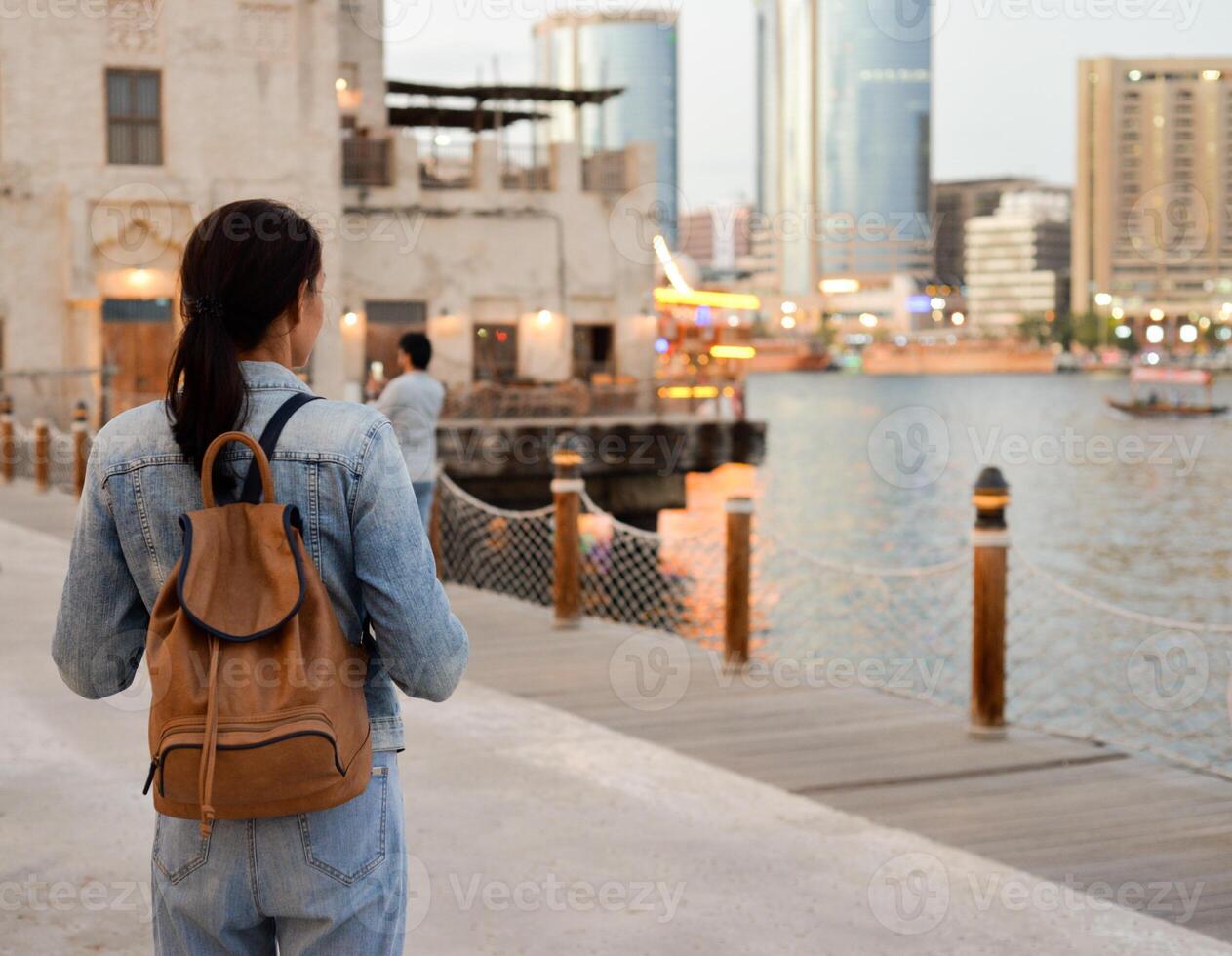 A young woman with a backpack on her back admires the river in the old Dubai Creek. Back view. Journey through the Persian Gulf photo