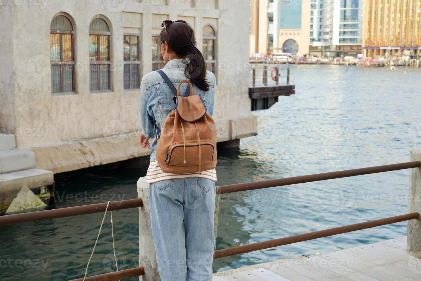 A young woman with a backpack on her back admires the river in the old Dubai Creek. Back view. Journey through the Persian Gulf photo