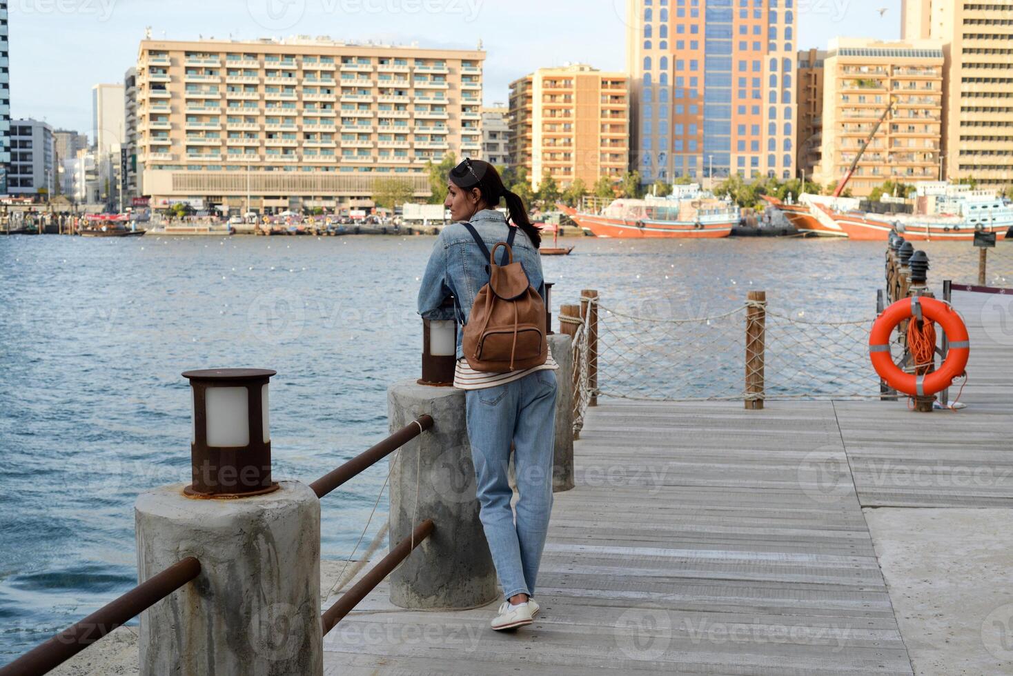 A young woman with a backpack on her back admires the river in the old Dubai Creek. Back view. Journey through the Persian Gulf photo