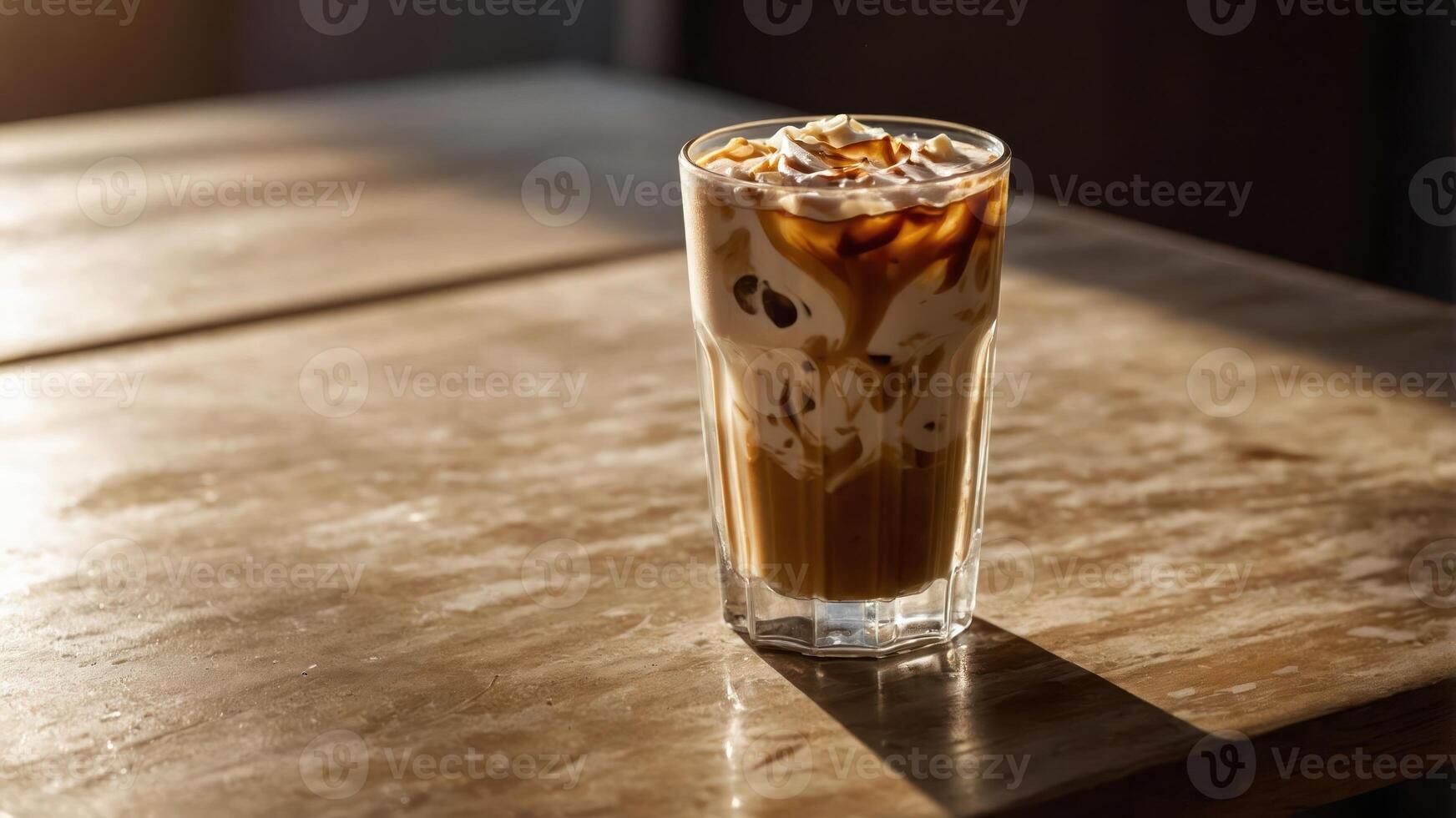 A glass of iced coffee with cream and caramel on a wooden table, illuminated by sunlight. photo