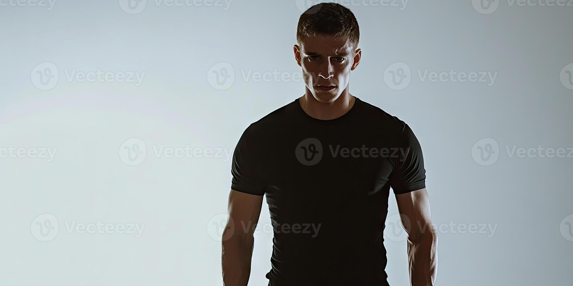 A man in a black T-shirt is standing in front of a white background, appearing unwell while posing. photo