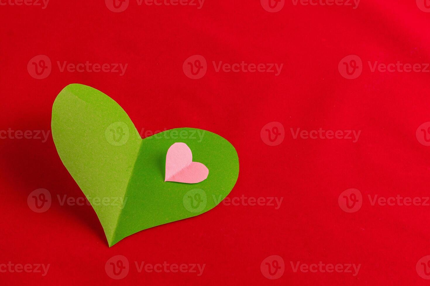 Green and pink heart cut out of paper on a red background photo