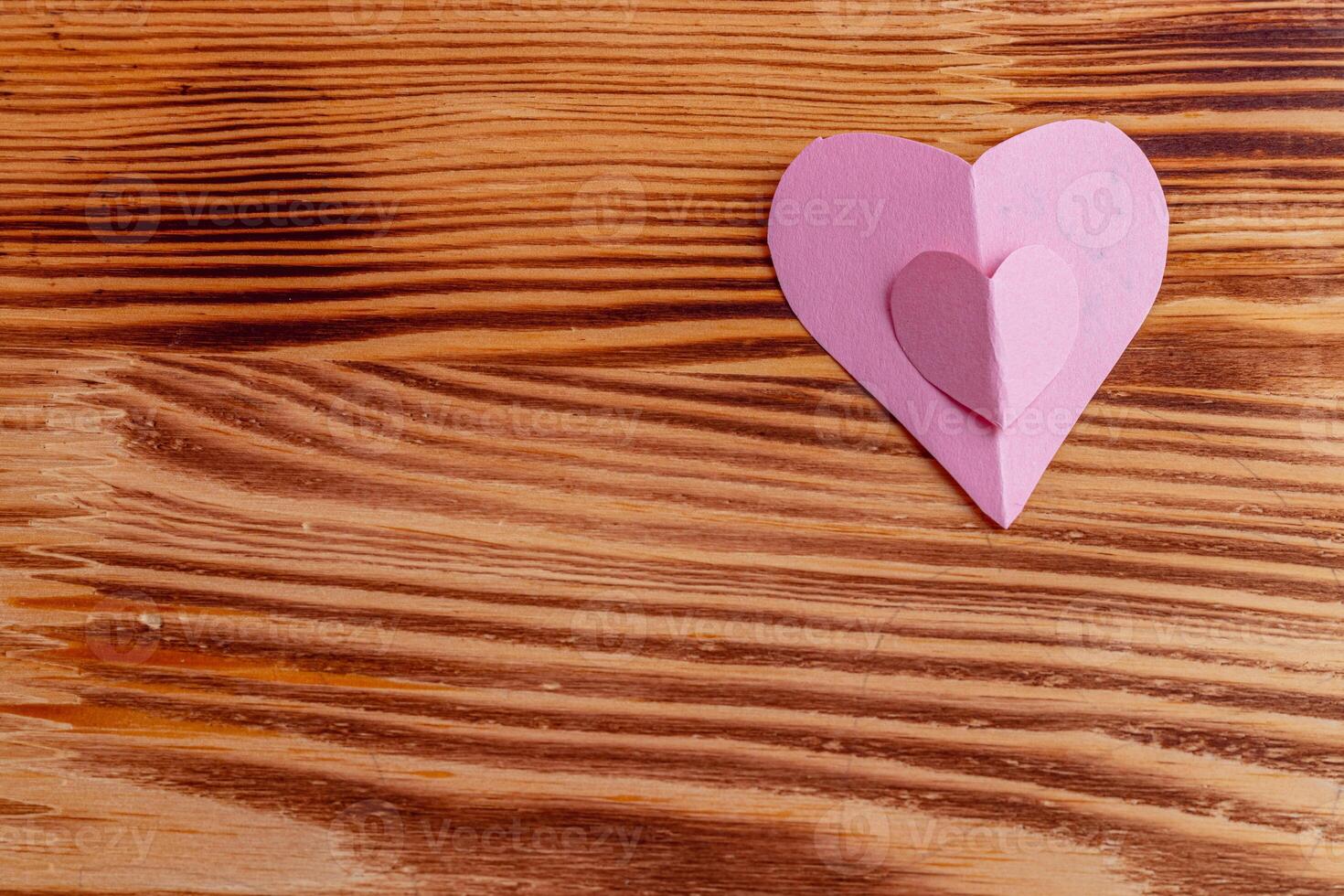 Hearts cut out of pink paper by hand on a wooden background photo