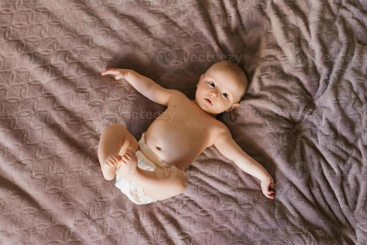 Cute sweet baby in a diaper lying on the bed on his back photo