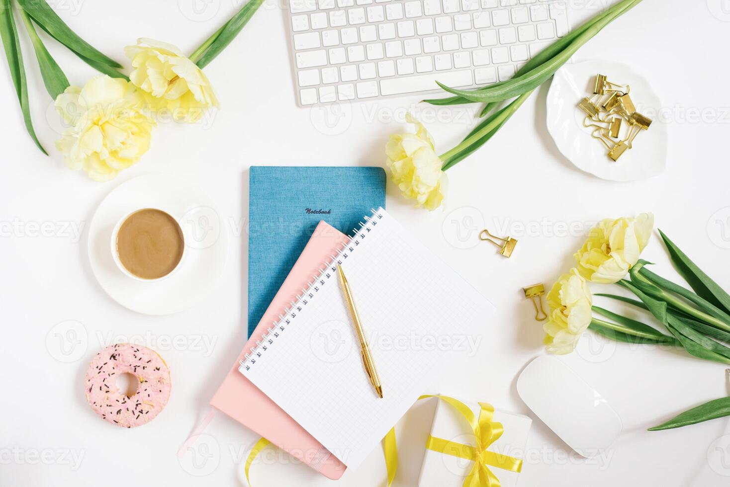 Office workspace with a white desk. Top view from above with a keyboard, notepad, gift, flowers and pencil with a white cup of coffee on a plate. Flat surface with copy space. Women's business concept photo