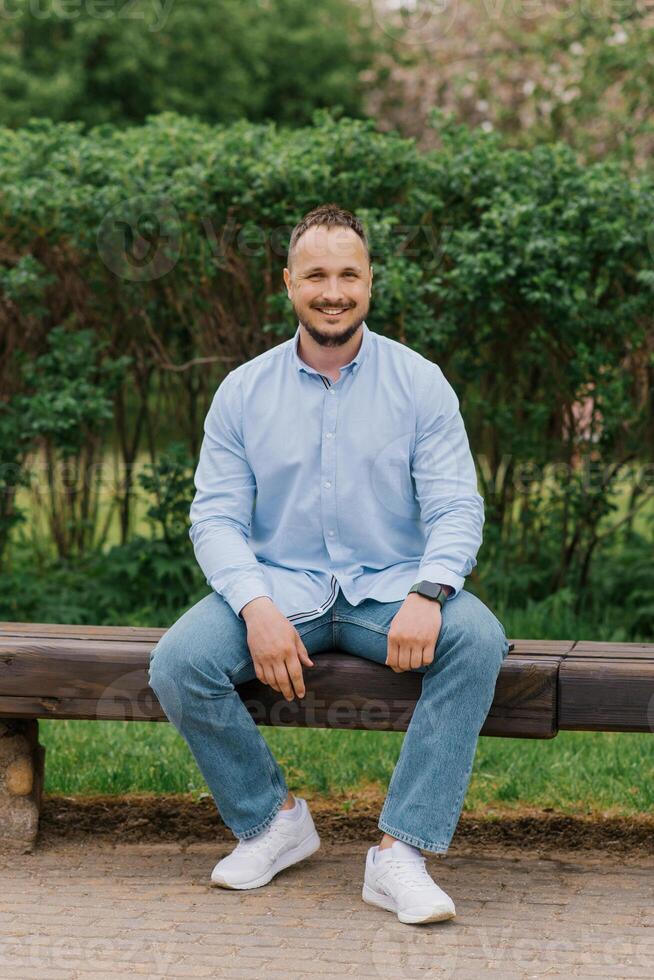 Attractive smiling man sitting alone on a park bench photo