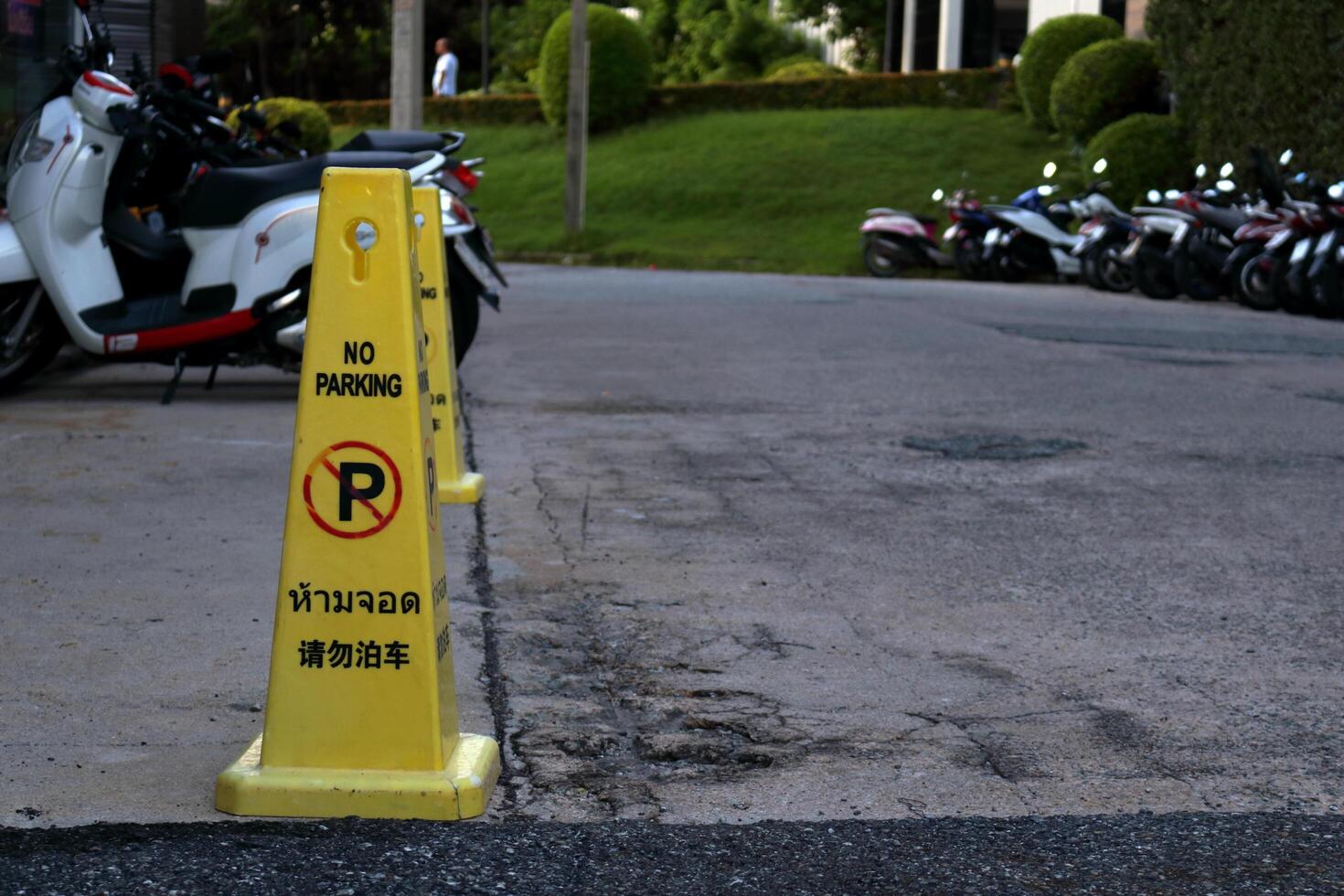 Yellow plastic cone with black letters word no parking three language Thai, English and Japanese on street front building. photo