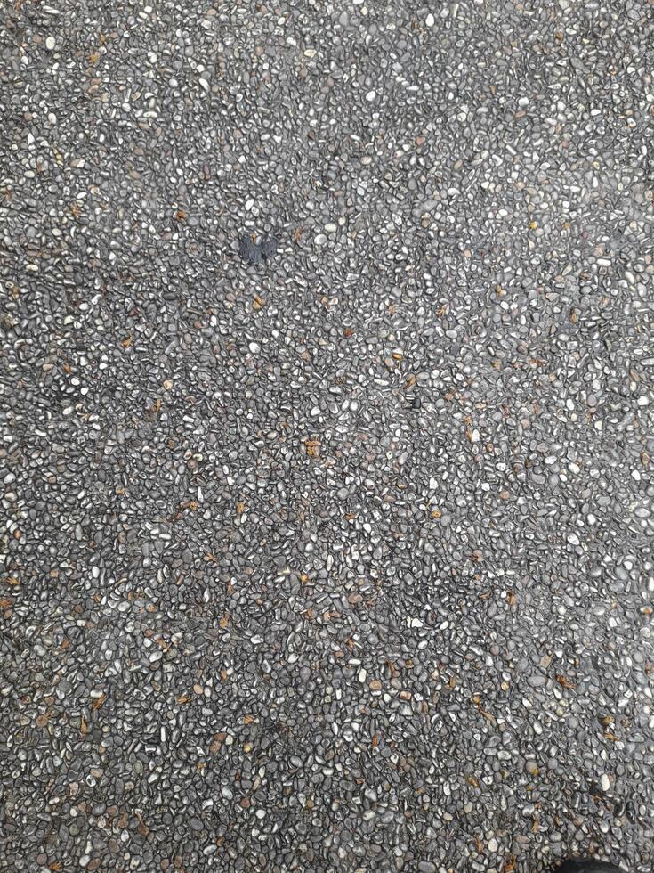A close-up view of an exposed aggregate concrete surface, consisting of small pebbles and stones embedded in a smooth, gray cement base. The texture is rough and detailed. photo