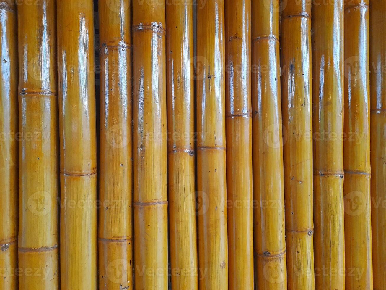 a display of polished golden brown bamboo stalks arranged vertically. The surface is smooth and glossy, with natural nodes in texture, showcasing the organic beauty of bamboo as a sustainable material photo