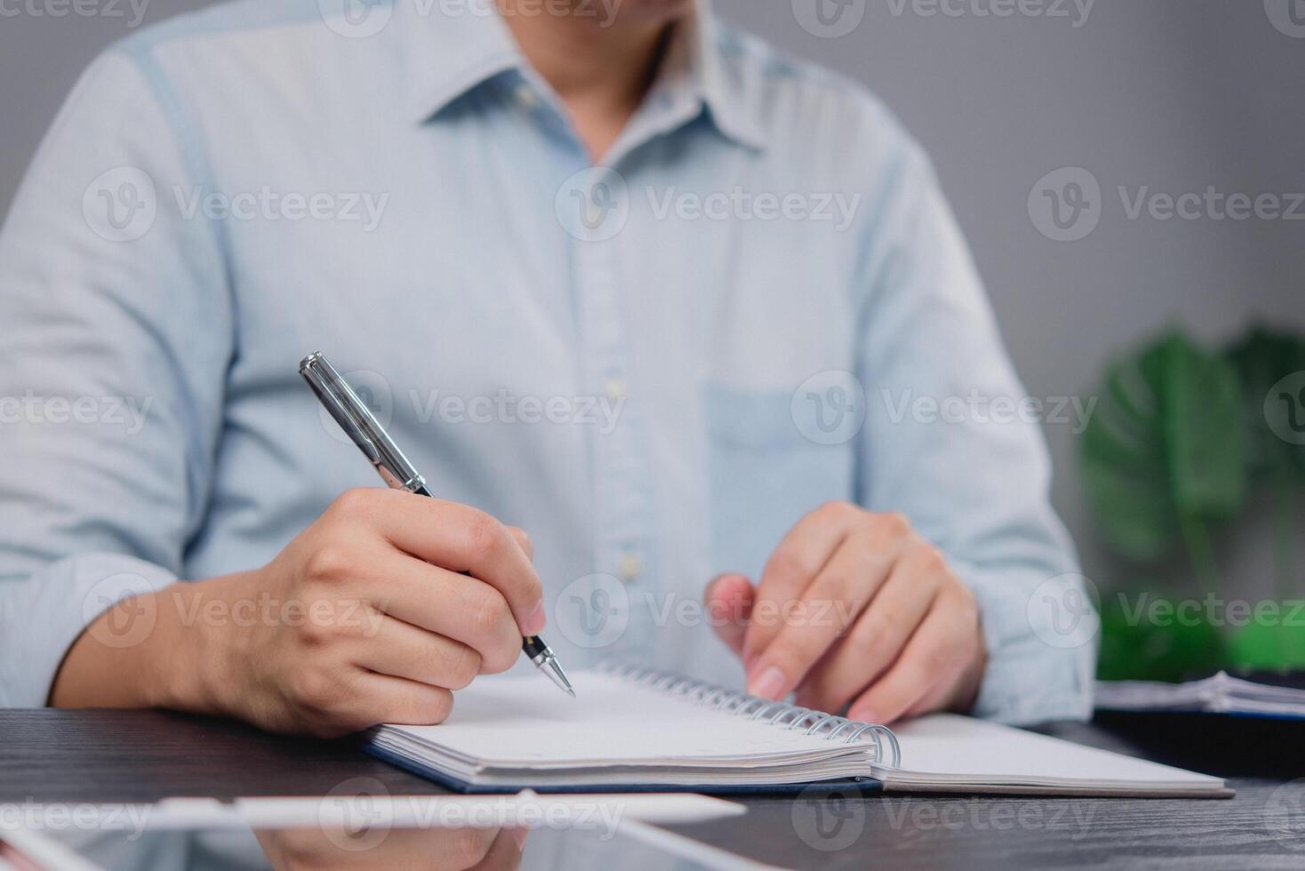 A man is writing in a notebook with a pen photo
