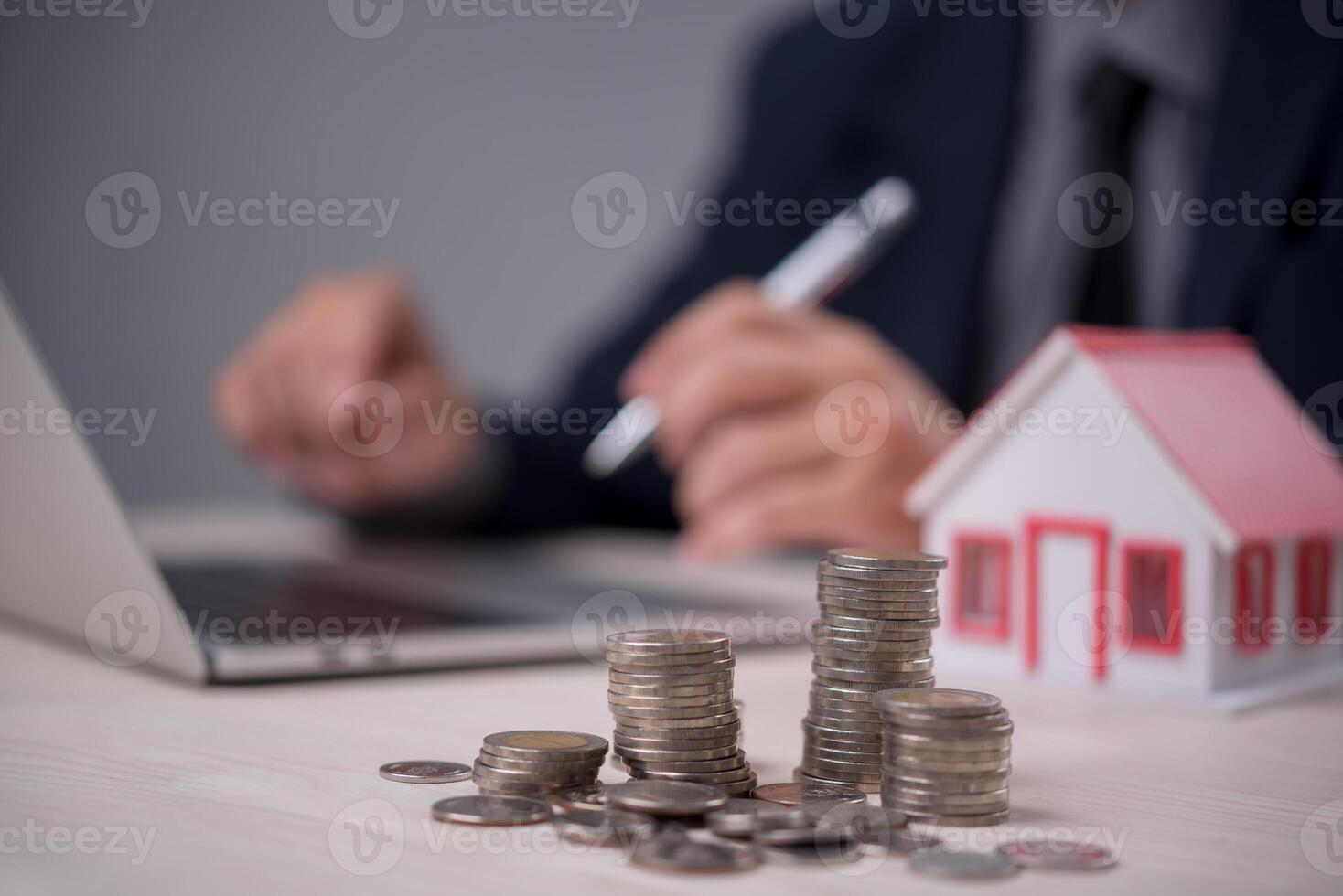 Man in suit sitting at desk with coins and house model photo