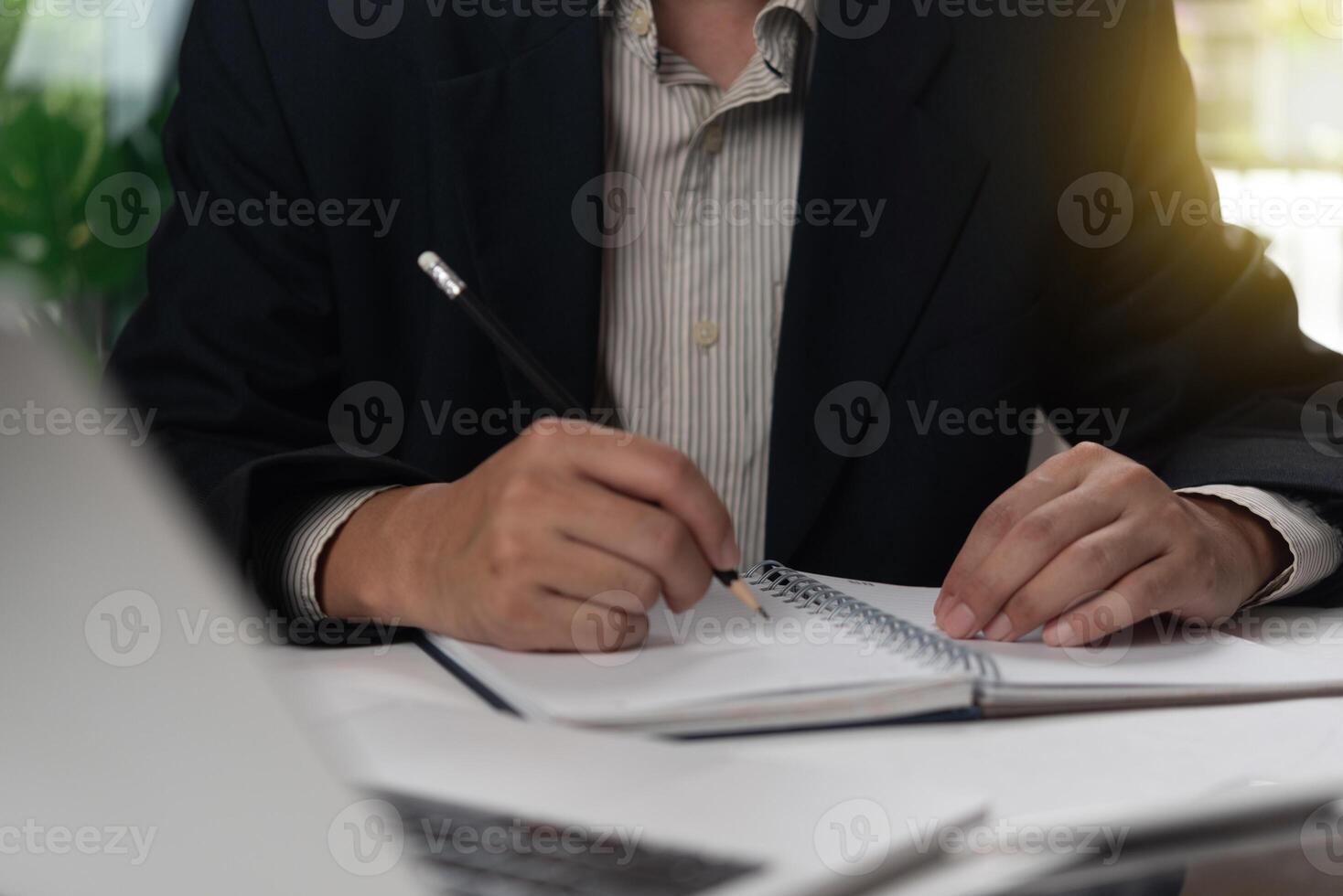 A man in a suit is writing on a notebook photo