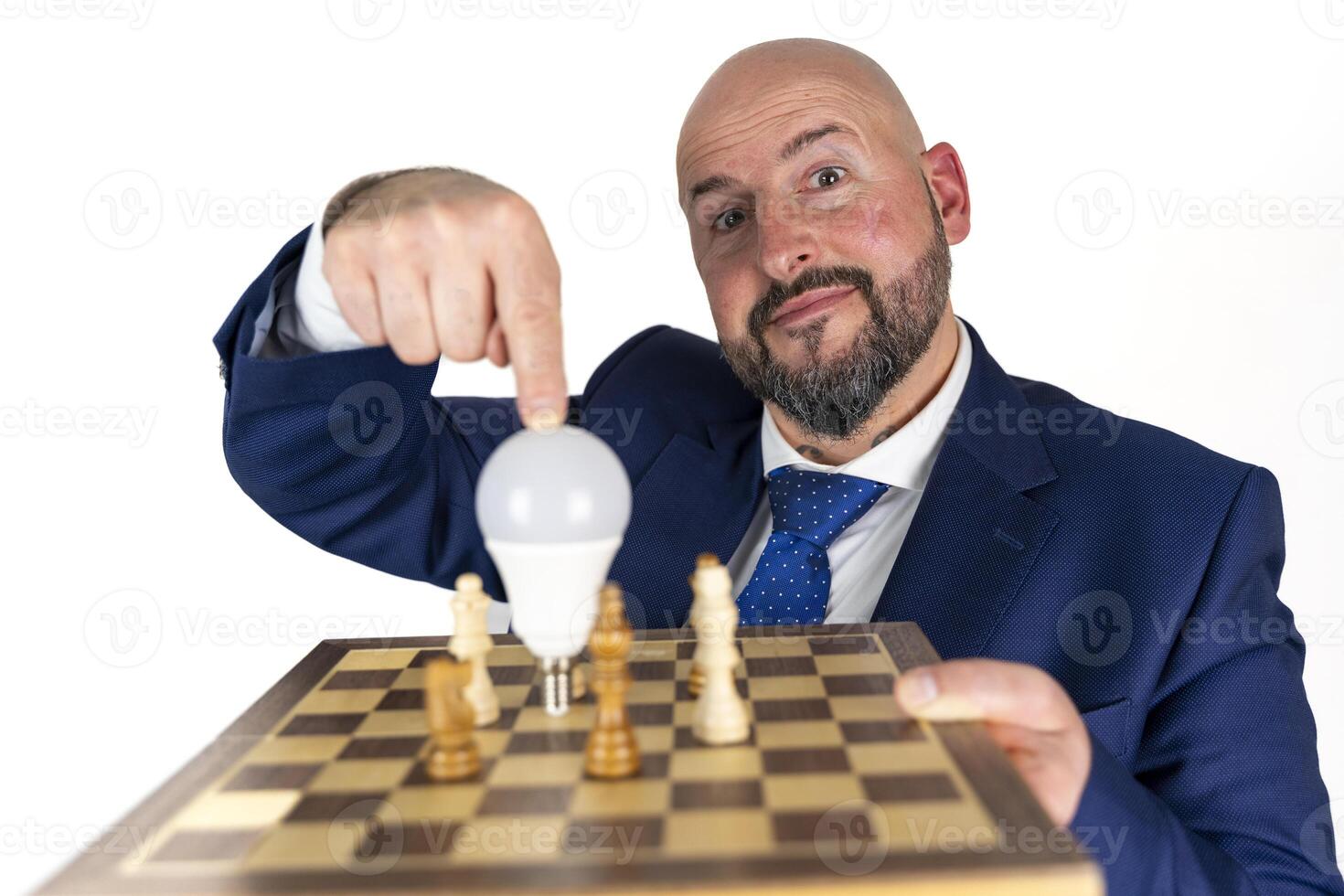 portrait of businessman in blue suit and tie with friendly expression showing light bulb on chessboard as symbol isolated on white background photo