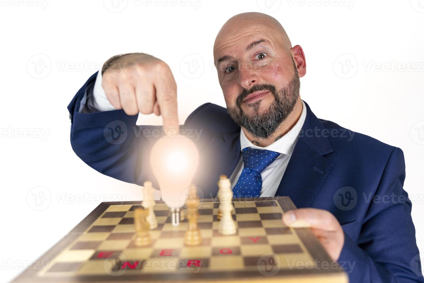 portrait of businessman in blue suit and tie with friendly expression showing light bulb on chessboard as symbol isolated on white background photo