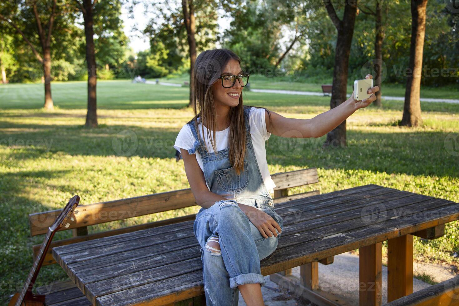 young smiling woman takes a selfie relaxing sitting on a table in public park photo