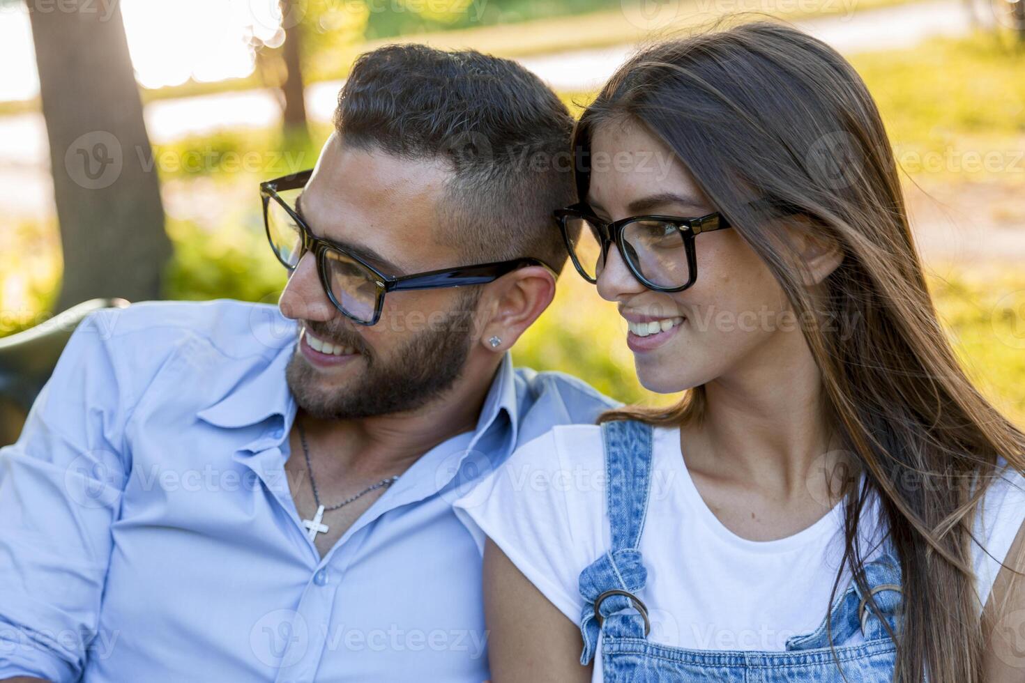 beautiful couple of young adult lovers smiling wearing eyeglasses relaxing sitting on table in park photo