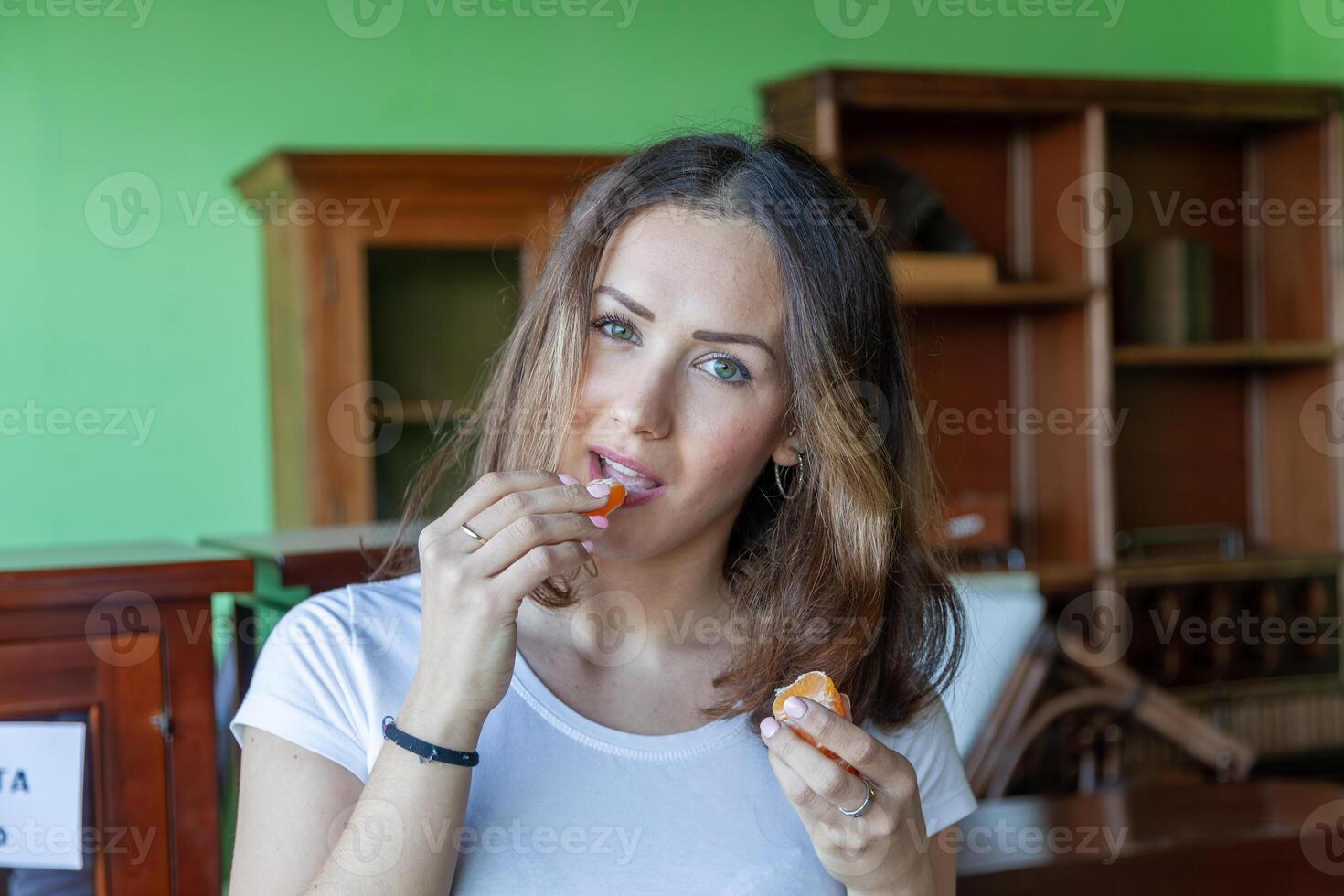 portrait of young beautiful woman is eating an orange in her house photo