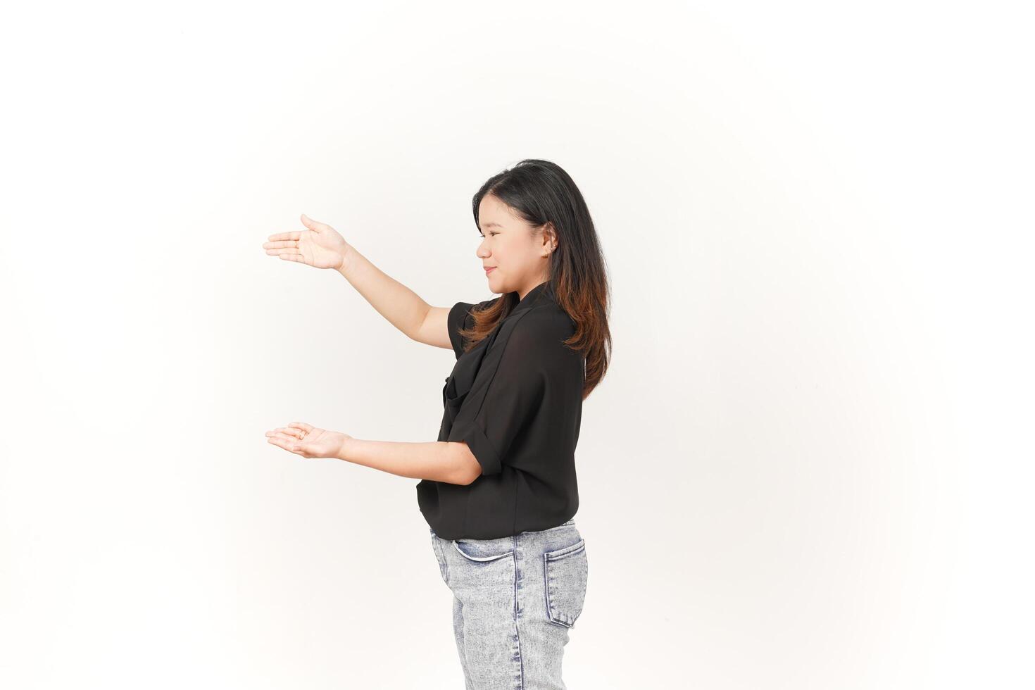 beautiful Asian woman poses with open hands, gesturing toward empty space to showcase a product against a white background photo
