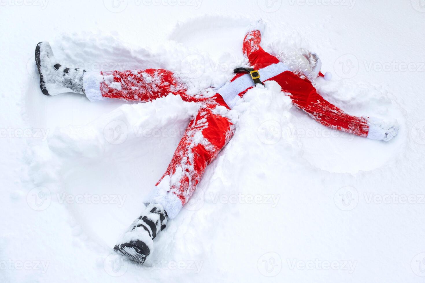 Santa Claus makes snow angels in the snow. Humor, winter fun, Santa is tired and drunk photo
