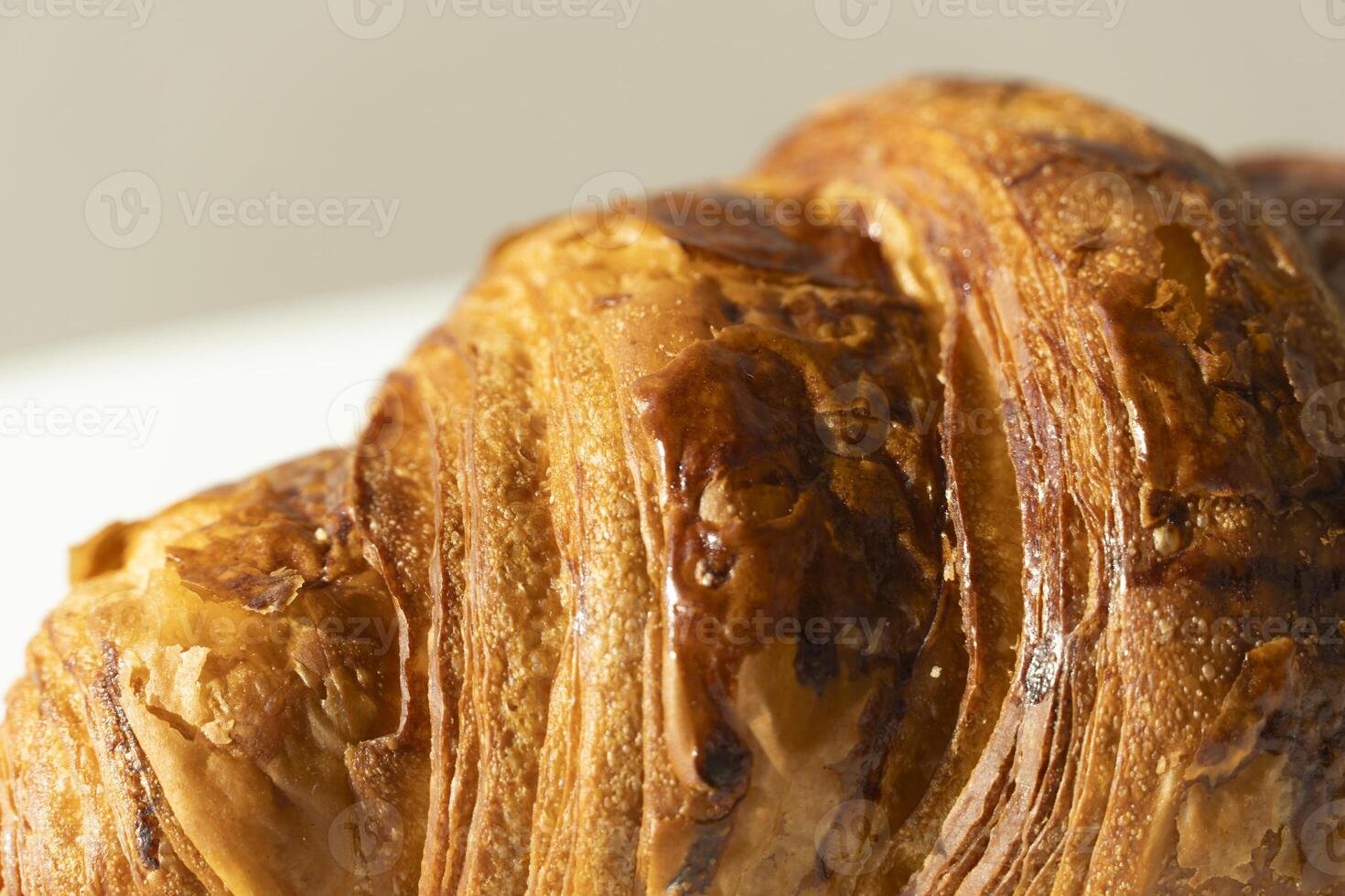 Freshly baked croissant on light background. Single French pastry closeup photo. Buttered bread croissant on white photo