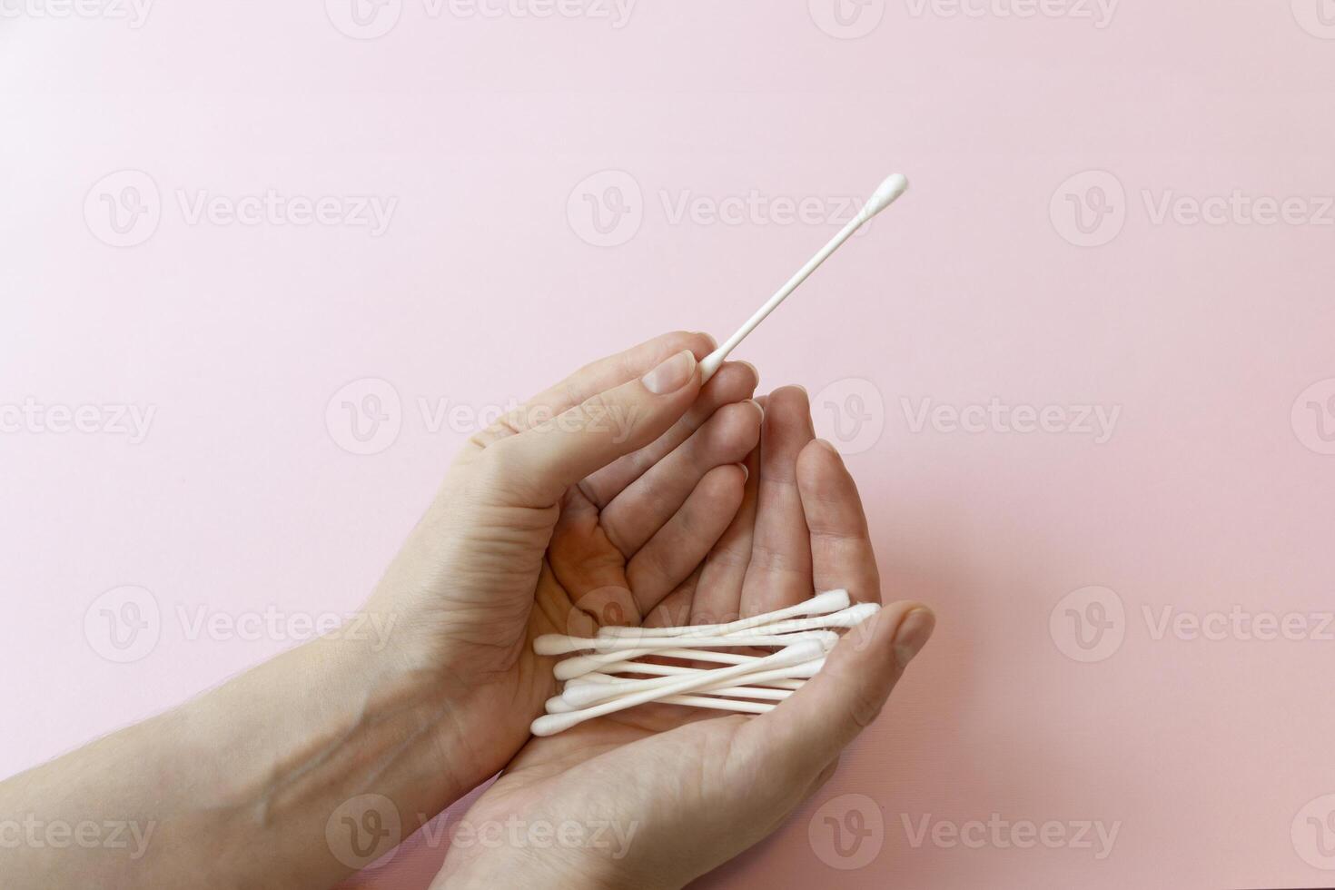 Cotton swab. Close up of woman's hand holding a cotton bud. Studio shot isolated on pink. Closeup of female hand holding cotton stick isolated on white photo