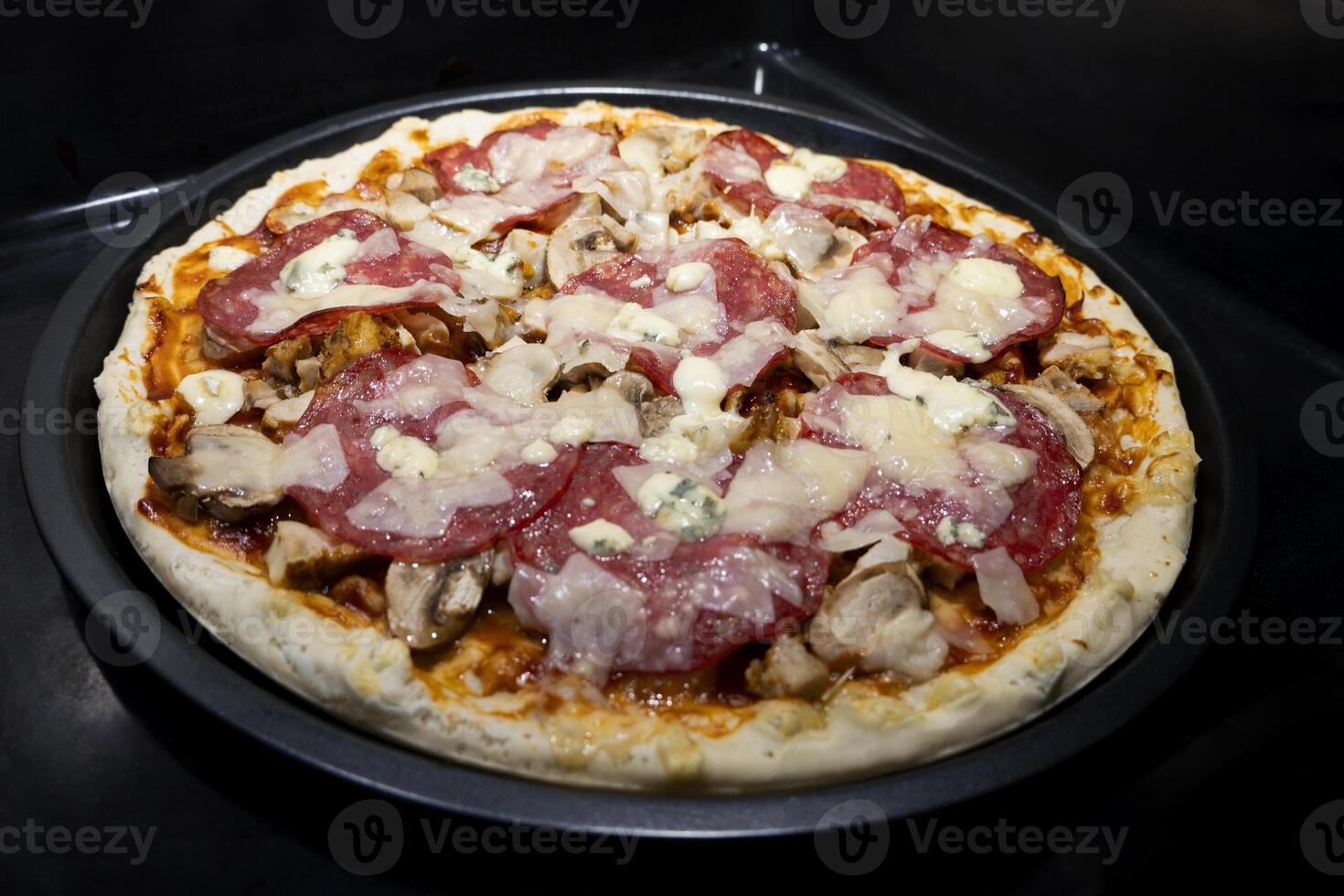 Pizza with cheese, salami, Tomato sauce, mushrooms, Flavors. Italian pizza on black surface. photo
