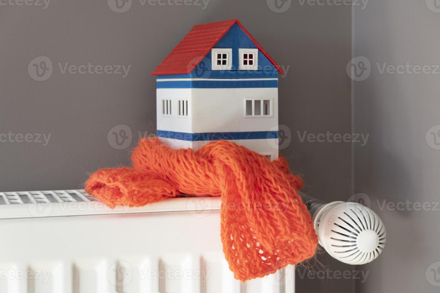 House model wrapped in scarf on radiator indoors. Winter heating efficiency photo