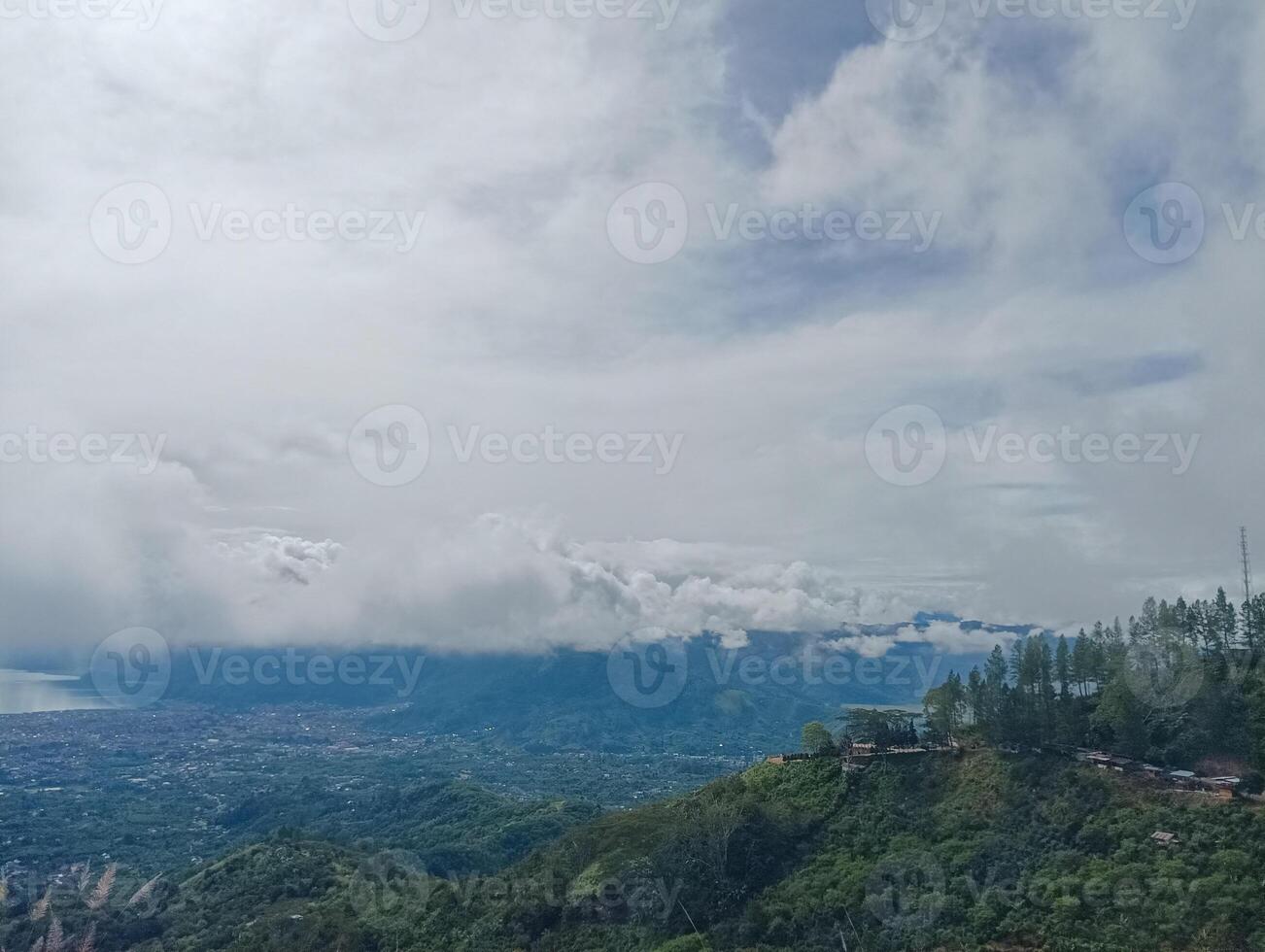 A scenic view of a lush green landscape with a lake surrounded by mountains under a cloudy sky. photo