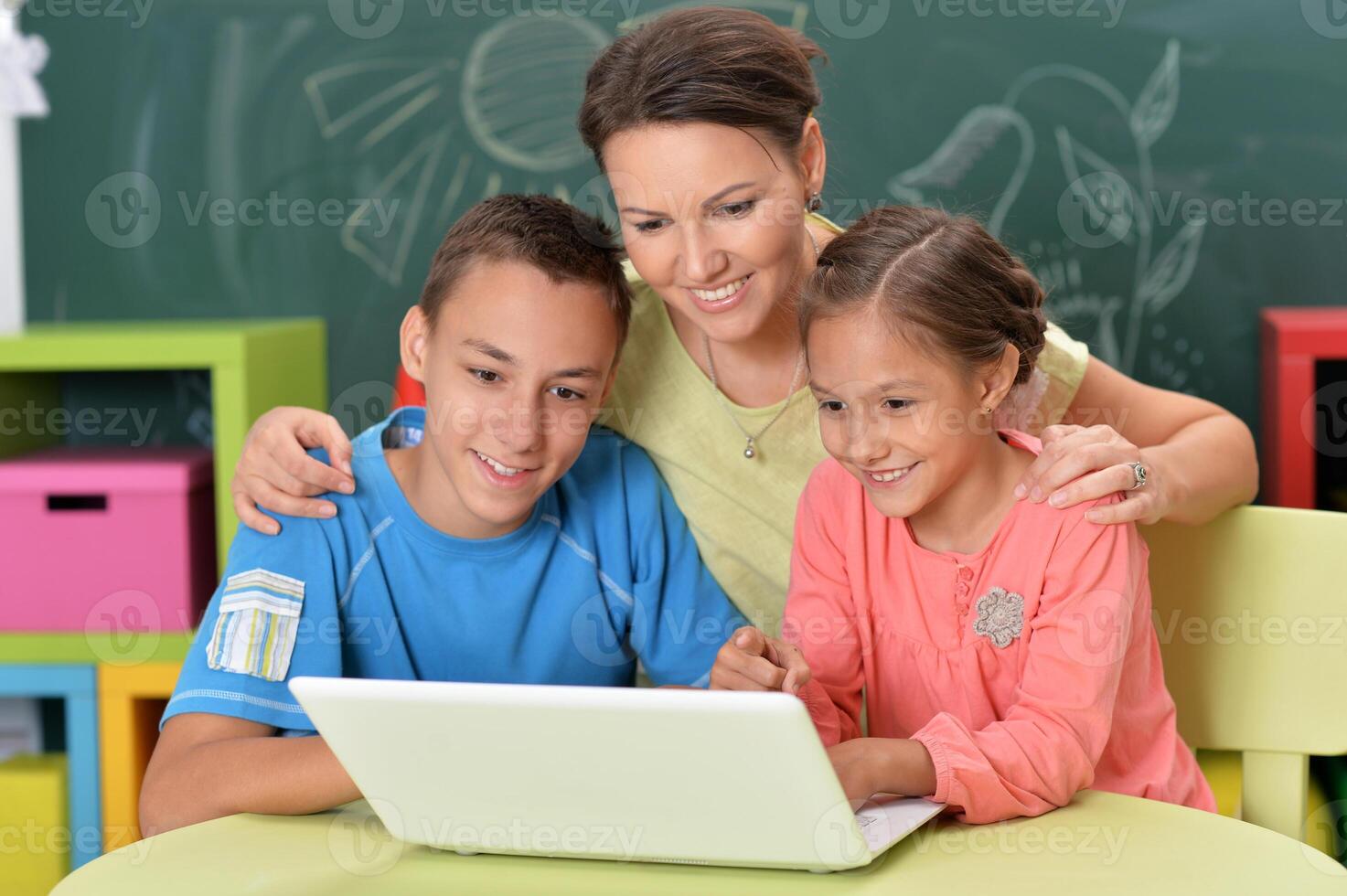Portrait of happy mother and children sitting at table with laptop photo