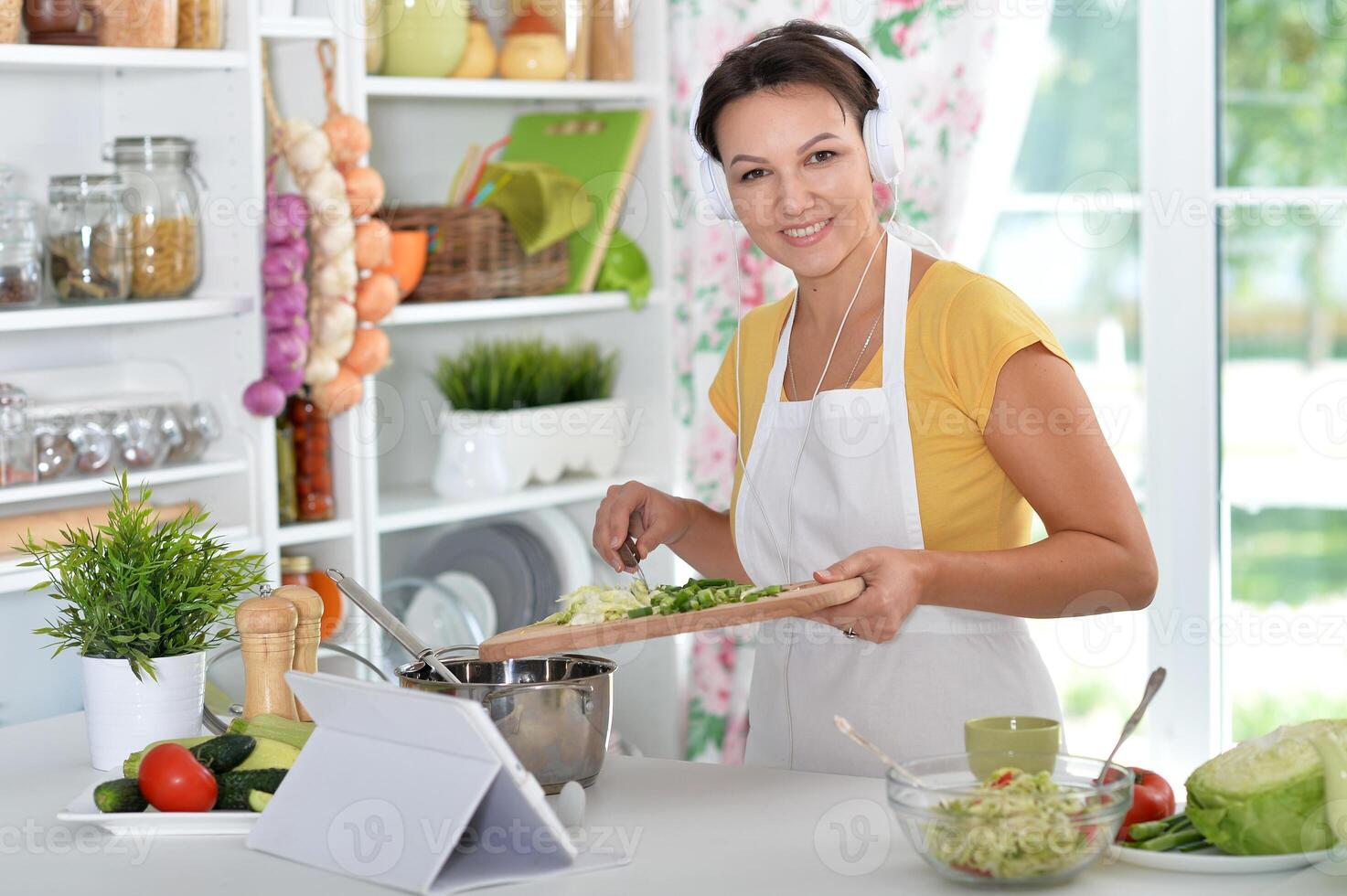 Portrait of beautiful young woman making salad and listening to music photo