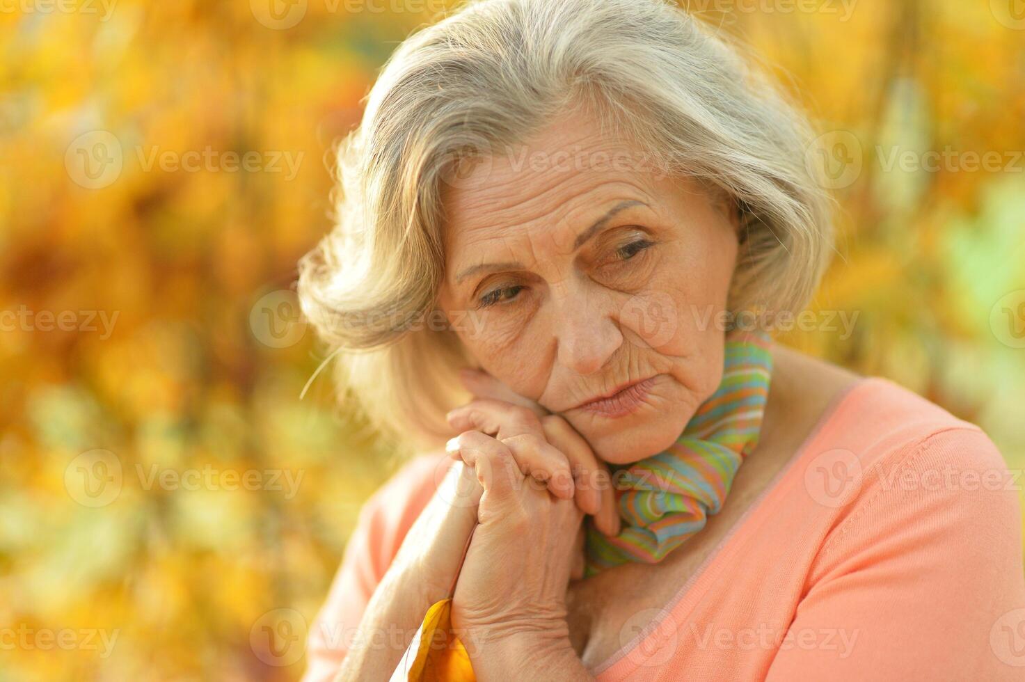 Portrait of beautiful sad senior woman on blurred autumn background photo