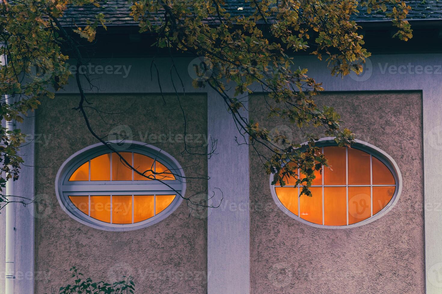 Illuminated oval windows are set into the textured facade of a building photo