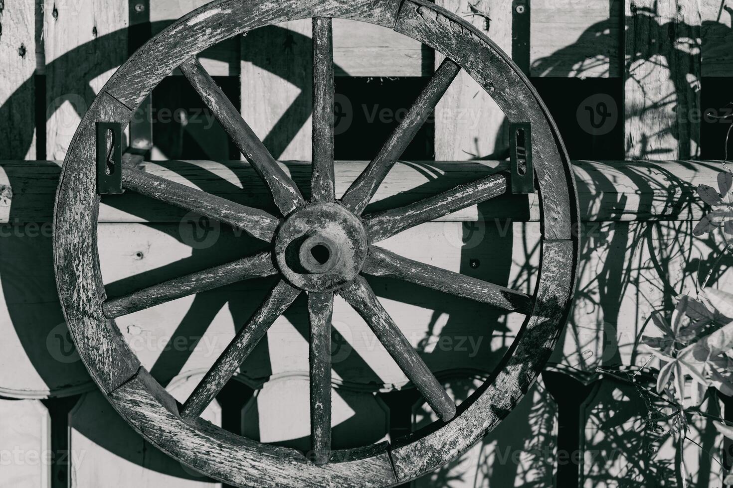 Rustic wooden wagon wheel mounted on a weathered wall in a quaint countryside setting during the afternoon sunlight photo
