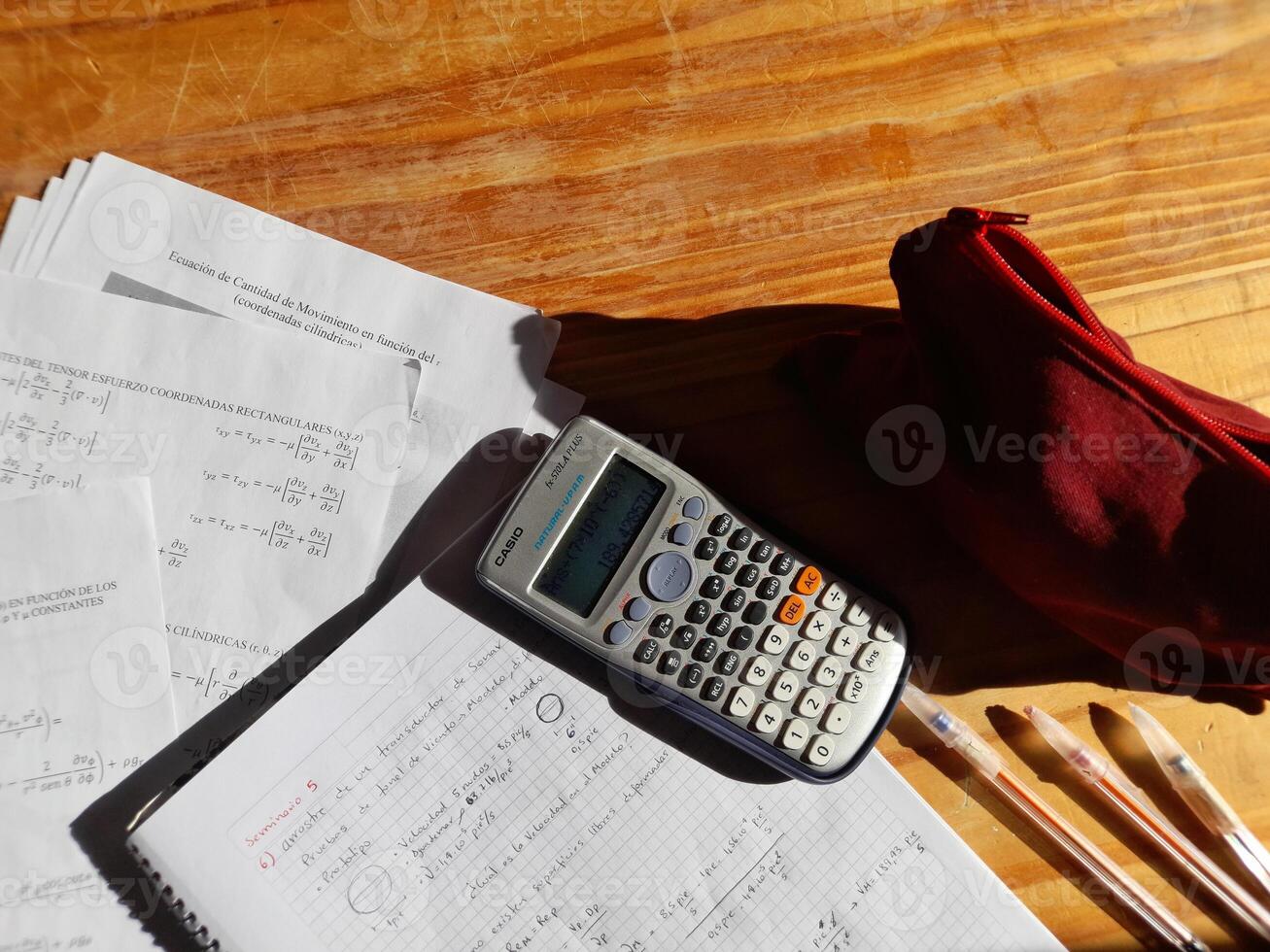 A calculator, red pen, and papers on a wooden table photo