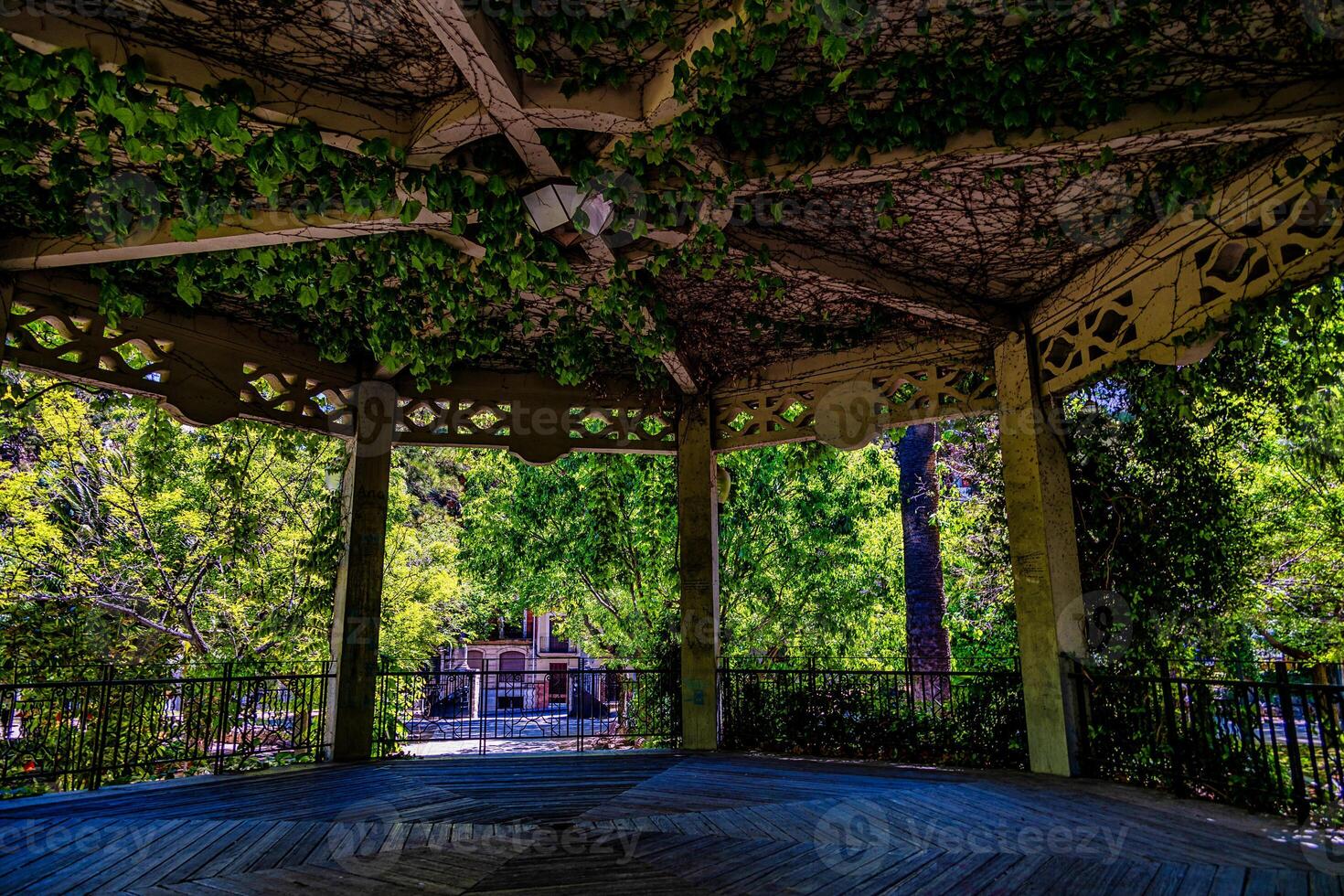 A wooden gazebo with intricate lattice work is adorned with lush green vines, creating a serene and shaded environment in Alcoy photo